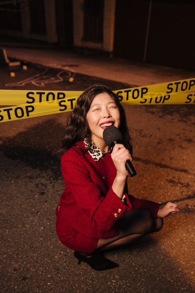 Asian reporter interviewing outdoors with microphone near barricade tape at night.